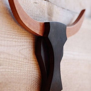 May include: A wooden bull head wall decor with brown horns and a black head. The head is mounted on a light wood background.