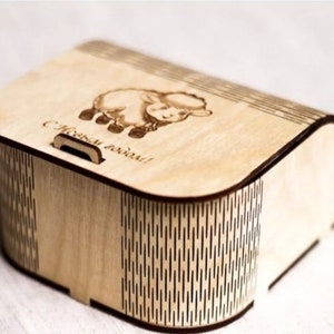 May include: A wooden box with a hinged lid and a cutout handle. The lid is decorated with a laser-engraved image of a sheep and the text "С Новым годом!" which translates to "Happy New Year!" in English. The box has a wood grain pattern and a decorative border.