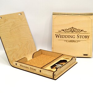 Peut inclure: Une boîte en bois avec un insert en liège et une fente pour une clé USB. La boîte est gravée des mots "Wedding Story" et présente un motif décoratif sur le couvercle.
