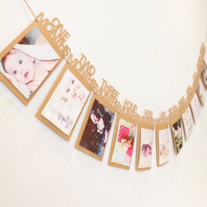 May include: A brown paper photo banner with gold glitter lettering that says "One Month, Two Months, Three Months, Four Months, Five Months, Six Months, Seven Months, Eight Months, Nine Months, Ten Months, Eleven Months, Twelve Months". Each month has a small photo frame attached to it.