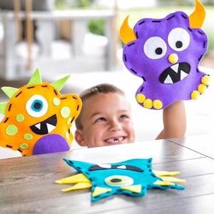 May include: Three felt monster hand puppets. One is purple with yellow horns and eyes, one is orange with green spikes and purple accents, and one is blue with yellow spikes and a green eye.