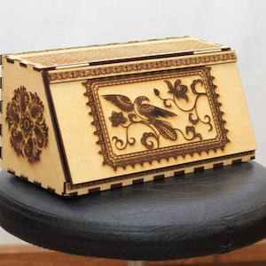 May include: A wooden bread box with a decorative floral and bird design. The box is made of light wood and has a hinged lid.