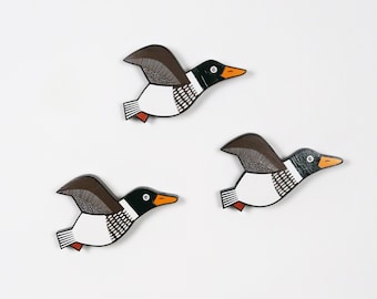 May include: Three wooden bird ornaments painted in black, white, and brown with orange accents. The birds are in a flying position with their wings spread out.