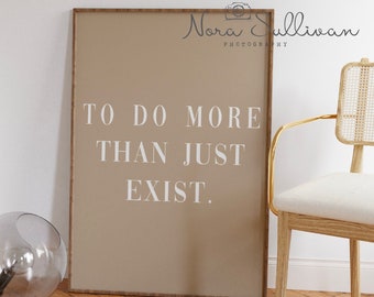 May include: A framed print with a beige background and white text that reads "To do more than just exist." The print is hanging on a wall with a wooden chair and a glass orb in the foreground.