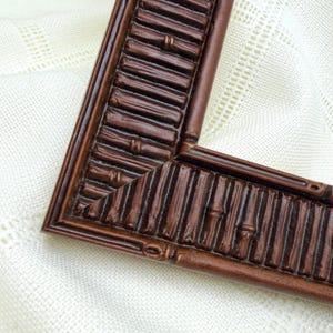 May include: A dark brown picture frame corner section featuring a textured, repeating bamboo-style pattern. The frame has a mitred joint where two segments meet, showcasing a consistent, raised, cylindrical design throughout the entire surface.