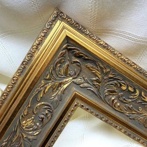 May include: An ornate picture frame corner featuring a metallic gold finish with dark grey recessed detailing. The frame displays a raised beaded outer edge and a central band decorated with intricate, embossed scrolling leaf patterns.
