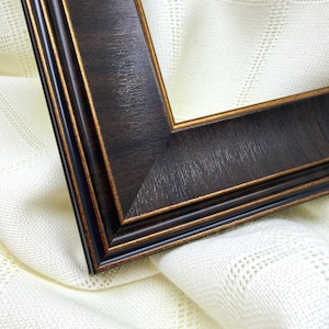 Peut inclure: Un cadre photo en bois brun foncé avec une texture de grain de bois visible et une fine bordure dorée le long des bords intérieurs et extérieurs. Le cadre présente un assemblage à onglet et un profil étagé avec plusieurs rainures.