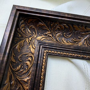 May include: A rectangular picture frame featuring a dark brown and metallic gold finish with an ornate, raised acanthus leaf scrollwork pattern. The inner edge displays a beaded texture, while the outer border has a smooth, angled profile.