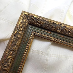 May include: An ornate picture frame featuring a dark green inner border and a raised, textured gold outer edge with intricate scrollwork patterns. The frame includes a thin, beaded gold trim detail along the inner perimeter of the frame.