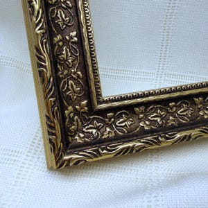 May include: An ornate picture frame featuring a dark brown recessed centre with a raised gold leaf ivy leaf pattern. The frame edges are finished with a bright gold metallic trim and a beaded border detail, creating a multi-layered appearance.