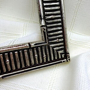 May include: A rectangular picture frame with a metallic silver finish and a dark, recessed background. The frame features a repeating vertical bamboo-like texture along its border, with a mitered corner joint and a distressed, weathered appearance.