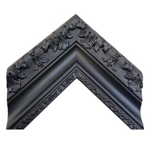 May include: A corner section of a black picture frame. The frame has ornate, raised floral and leaf detailing along the outer edge and inner corners. The frame is a matte black color.