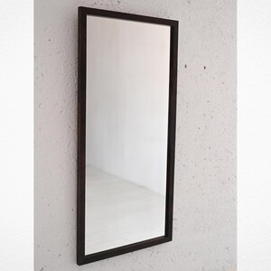 Può includere: Uno specchio rettangolare con una cornice in legno marrone scuro. Lo specchio è appeso a una parete bianca.