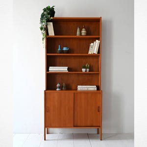Librería escandinava de teca de los años 60 con estantes abiertos y carpintería vista: almacenamiento moderno de mediados de siglo