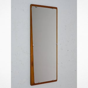 Puede incluir: Un espejo rectangular con marco de madera de color marrón claro. El espejo está colgado en una pared blanca.