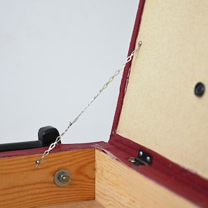 K&ouml;nnte beinhalten: Eine rote Holzkiste mit einem Scharnierdeckel und einer Metallkette, die am Deckel befestigt ist. Die Kiste ist ge&ouml;ffnet und das Innere ist mit Holz ausgekleidet.