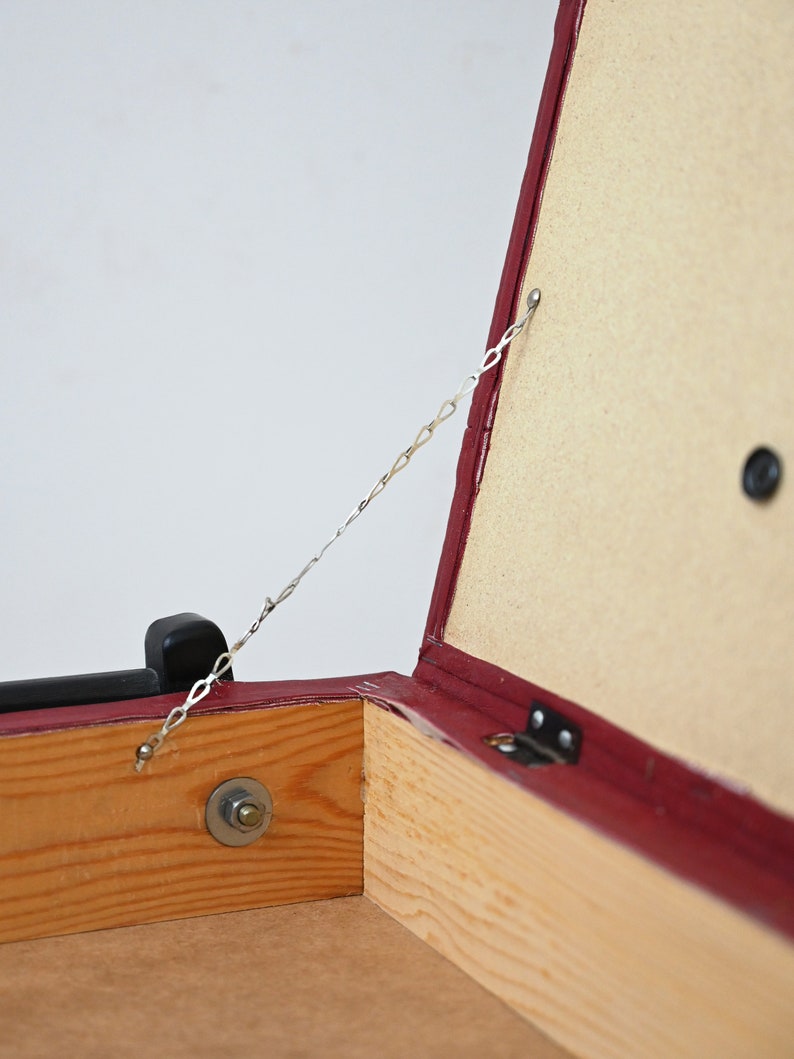 K&ouml;nnte beinhalten: Eine rote Holzkiste mit einem Scharnierdeckel und einer Metallkette, die am Deckel befestigt ist. Die Kiste ist ge&ouml;ffnet und das Innere ist mit Holz ausgekleidet.