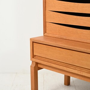 May include: A light-colored wooden cabinet with three drawers and a lower drawer. The drawers have a unique, curved design. The cabinet is supported by four legs and is set against a white background. The wood has a natural finish.