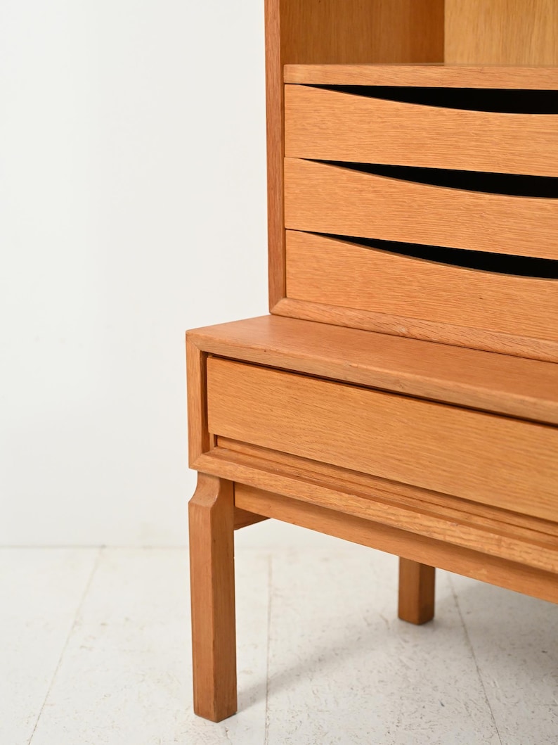 May include: A light-colored wooden cabinet with three drawers and a lower drawer. The drawers have a unique, curved design. The cabinet is supported by four legs and is set against a white background. The wood has a natural finish.