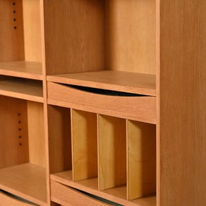 May include: A light brown wooden bookcase with multiple shelves and compartments. The bookcase has a natural wood grain finish and a simple, modern design. The shelves are of varying sizes, and some have curved edges. The bookcase is likely used for storage and display.