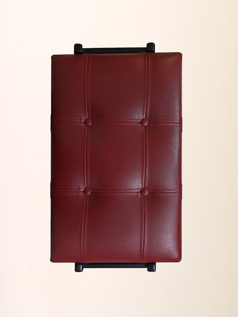 K&ouml;nnte beinhalten: Eine rote Klavierbank aus Leder mit einem gesteppten Design und schwarzen Metallbeinen.