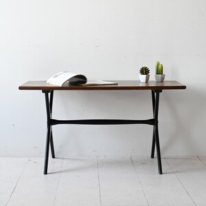 Op de afbeelding: Een bruine houten tafel met zwarte metalen poten. De tafel heeft een tijdschrift erop en twee kleine potplanten.