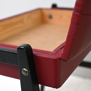 K&ouml;nnte beinhalten: Ein roter Polsterstuhl mit schwarzen Holzbeinen. Der Stuhl hat einen Holzrahmen und eine rote Ledersitzfl&auml;che und -lehne.