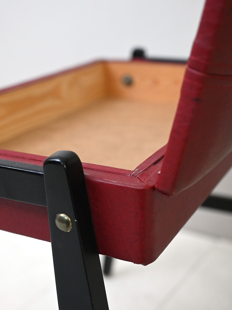K&ouml;nnte beinhalten: Ein roter Polsterstuhl mit schwarzen Holzbeinen. Der Stuhl hat einen Holzrahmen und eine rote Ledersitzfl&auml;che und -lehne.