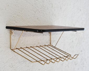 May include: A gold metal shelf with a black wooden top. The shelf has a wire rack underneath for storage.