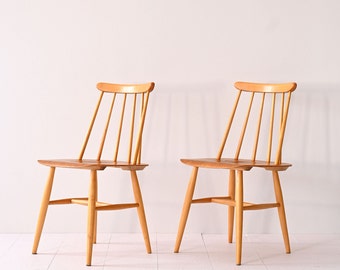 Könnte beinhalten: Zwei Holzstühle mit schlichtem, klassischem Design. Die Stühle haben eine helle Holzoptik und eine Lattenrücklehne.