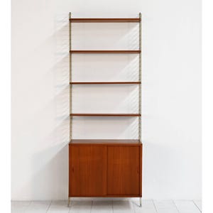 May include: A tall, mid-century modern shelving unit with a warm wood finish. The unit features four shelves and a lower cabinet with two doors. The vertical supports are a light metal color, and the unit stands on four metal legs.