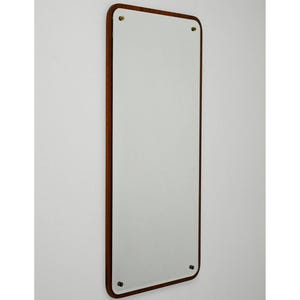 Può includere: Uno specchio rettangolare con angoli arrotondati, incorniciato in legno marrone scuro. Lo specchio è montato su una parete bianca con viti color ottone. Il design è semplice ed elegante, adatto a vari stili di interni.