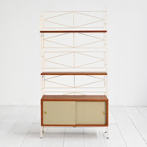 May include: A mid-century modern shelving unit with a white metal frame and wooden shelves. The unit features a cabinet with sliding doors at the bottom and open shelves above. The shelves are a warm brown color, and the cabinet doors are a light beige.