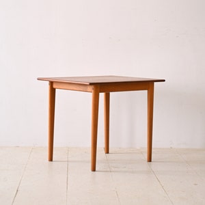 May include: A square wooden table with four legs. The table is made of light brown wood and has a simple design.