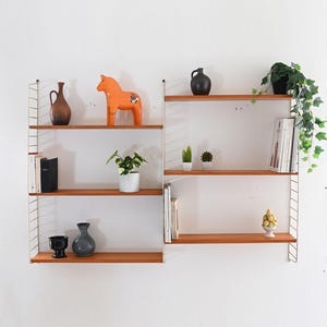 May include: A vintage wall-mounted shelving unit with wooden shelves and white metal supports. The shelves are adorned with decorative items such as vases, a ceramic horse figurine, potted plants, and books. The unit is mounted on a white wall.