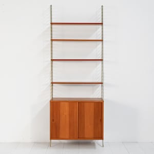 May include: A mid-century modern wall-mounted shelving unit. The unit features a wooden cabinet with sliding doors at the bottom, four shelves, and a metal frame. The wood has a warm, reddish-brown tone.