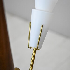 Może przedstawiać: Złota metalowa lampa z dwoma białymi, stożkowymi kloszami. Lampa ma zakrzywiony wysięgnik i drewnianą podstawę.