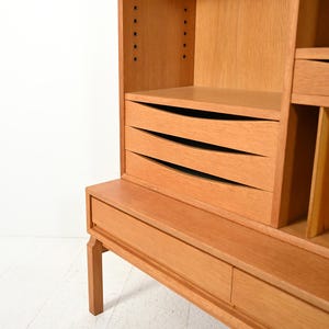 May include: A light brown wooden cabinet with multiple shelves and drawers. The cabinet has a rectangular shape with a flat top and a base with a single drawer. The drawers have curved fronts. The cabinet is made of wood and has a natural finish.