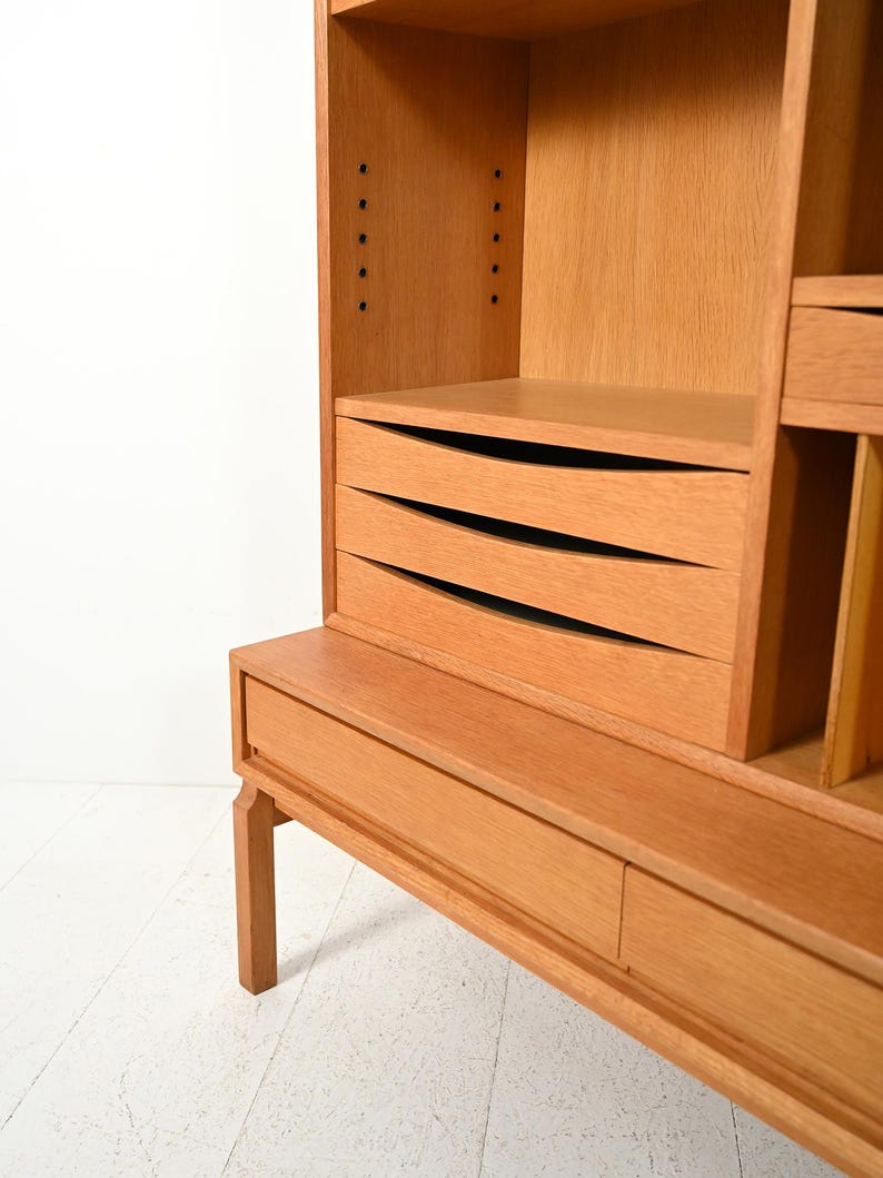 May include: A light brown wooden cabinet with multiple shelves and drawers. The cabinet has a rectangular shape with a flat top and a base with a single drawer. The drawers have curved fronts. The cabinet is made of wood and has a natural finish.