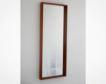 May include: A rectangular mirror with a dark brown wooden frame. The mirror is mounted on a white wall. The frame is a simple, clean design, and the mirror itself reflects the surrounding environment.