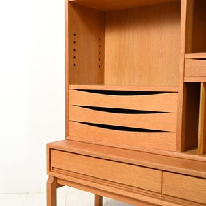 May include: A light brown wooden cabinet with multiple shelves, drawers, and a lower cabinet. The cabinet has a mid-century modern design with clean lines and a natural wood finish. The drawers have curved, black-lined accents.