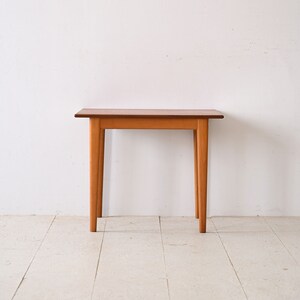 May include: A simple wooden table with a light brown finish and four legs. The table is sitting on a white floor.