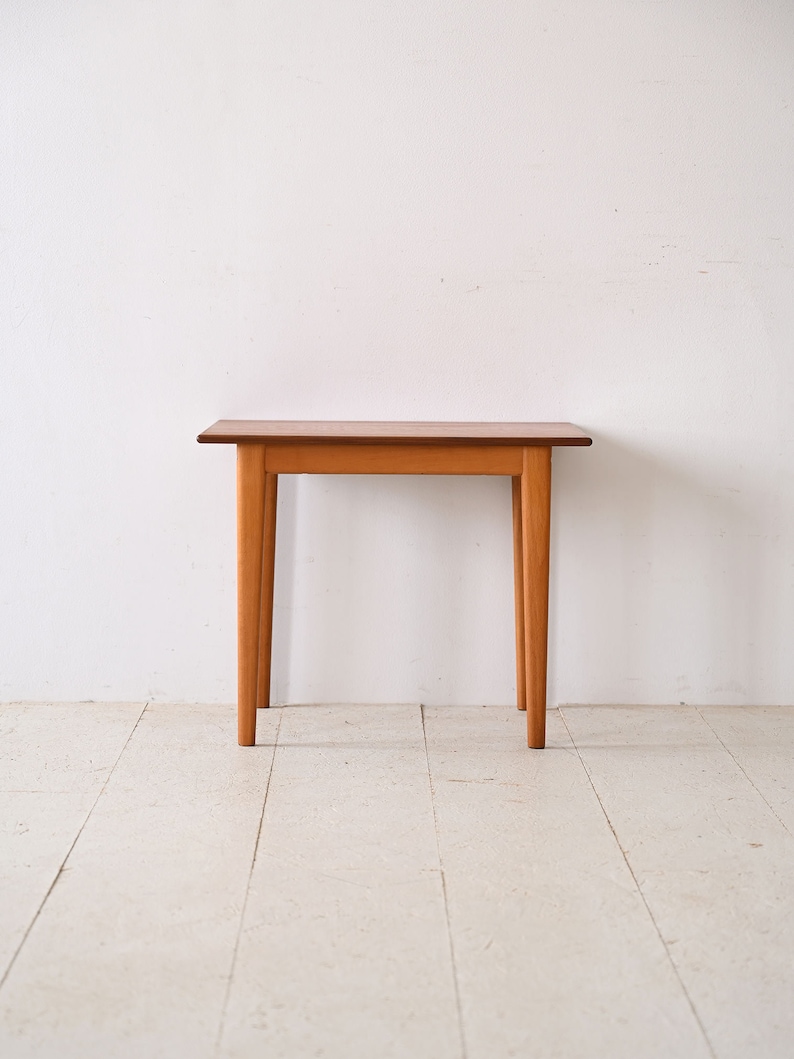 May include: A simple wooden table with a light brown finish and four legs. The table is sitting on a white floor.