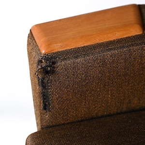 Pu&ograve; includere: Primo piano di una sedia in tessuto marrone con una parte superiore in legno. La sedia ha una tappezzeria in tessuto marrone con una texture sottile. La parte superiore della sedia &egrave; in legno marrone chiaro.