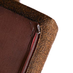 Pu&ograve; includere: Primo piano di un cuscino per sedia in tessuto marrone e oro con una cerniera. La cerniera &egrave; aperta e il cuscino &egrave; fatto di un tessuto strutturato.