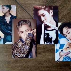 May include: A collection of five rectangular photo cards featuring images of young men. The cards display various poses, including one with a dog, and different outfits. The cards are arranged on a brown wooden surface.