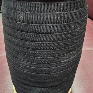 May include: A spool of black cotton twill tape. The tape is woven in a herringbone pattern and is wound tightly on the spool.