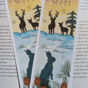 Peut inclure: Deux modèles de signets avec une illustration aquarelle d'un lapin, d'un cerf et d'un plus petit cerf dans un décor de forêt enneigée. Le haut de chaque signet présente le mot "SMMM" dans une police de caractères stylisée.