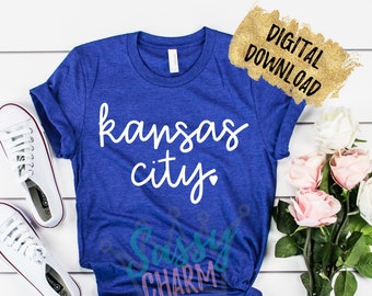 Może przedstawiać: Królewsko-niebieska koszulka z napisem "Kansas City" w białym skrypcie. Koszulka jest zawiązana na dole i znajduje się obok białych trampek i różowych róż. Złota grafika do pobrania cyfrowego znajduje się w prawym górnym rogu.