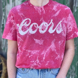 May include: Red t-shirt with a white bleach tie-dye pattern and the word "Coors" printed in white.